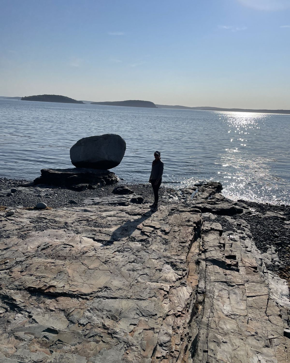 A traveler standing on a rocky shoreline looking out over calm water and distant islands